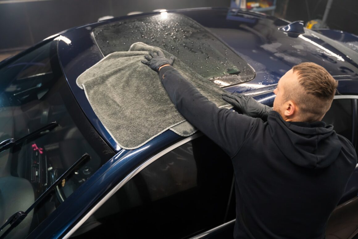 Car wash worker wipes the car after washing with microfiber towel. Professional car wash