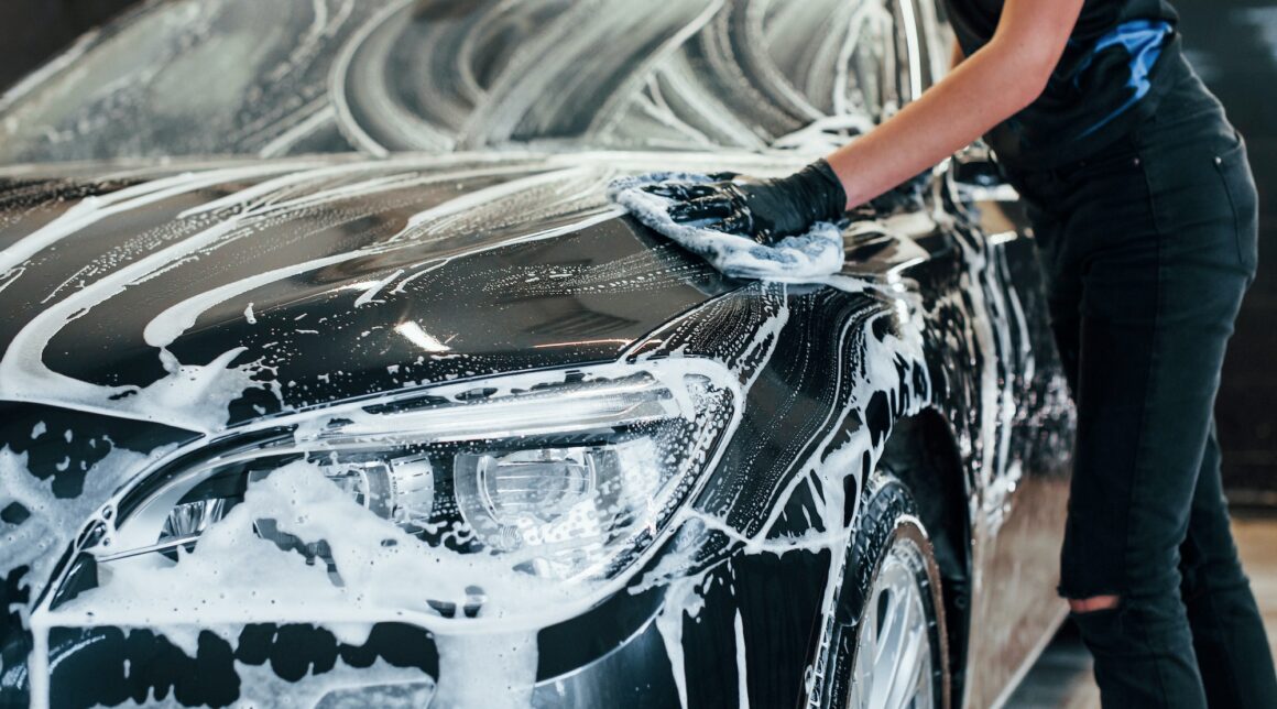 Modern black automobile get cleaned by woman inside of car wash station